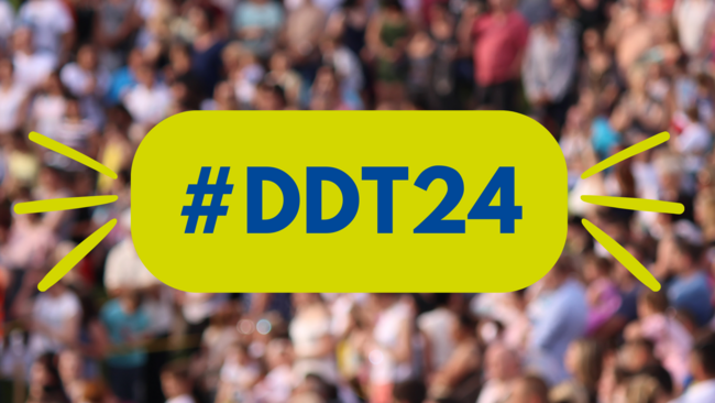 In einem Textfeld steht "DDT24". Im Hintergrund ist eine verschwommene Menschenmenge.