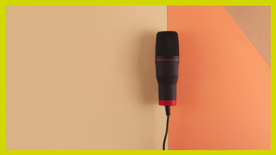 Symbolbild: Ein Mikrofon liegt mittig im Bild, dahinter orangener Grund. 